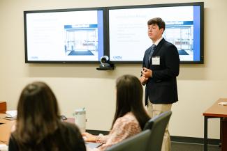 A student presents their sales pitch to a room of corporate partners.