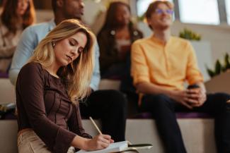 Focused student taking notes during conference in modern lecture hall