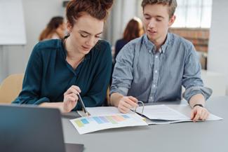 two students are looking at charts to apply economic principles to their next assignment.