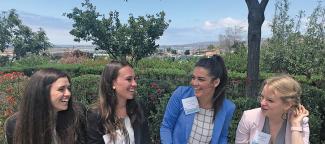 A group of four colleagues and students happily discussing social entrepreneurship outside in a hedge garden on a park bench.