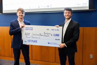 Two professional students hold up a large prize check for $4,000 for winning first place in the stock pitch competition.
