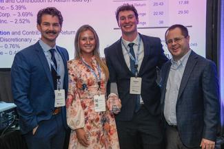 Four people dressed in formal attire stand smiling at an event. One person holds an award. A presentation screen displays company names like Apple Inc. and Microsoft Corp. behind them. The award has the Tennessee Valley Authority logo on it.