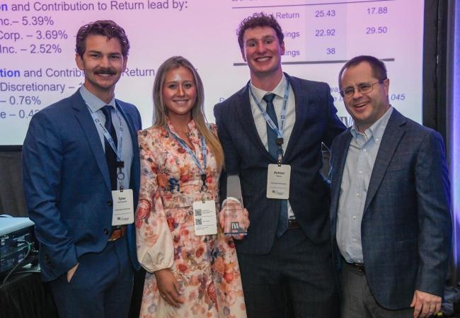 Four people dressed in formal attire stand smiling at an event. One person holds an award. A presentation screen displays company names like Apple Inc. and Microsoft Corp. behind them. The award has the Tennessee Valley Authority logo on it.