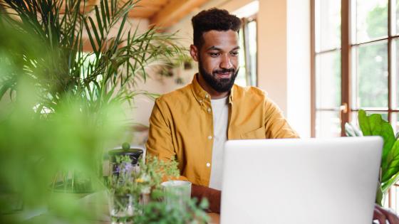 Young man with laptop and coffee working indoors, home office concept.