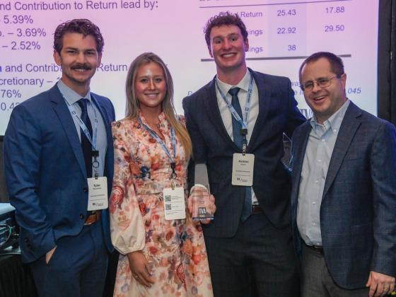 Four people dressed in formal attire stand smiling at an event. One person holds an award. A presentation screen displays company names like Apple Inc. and Microsoft Corp. behind them. The award has the Tennessee Valley Authority logo on it.