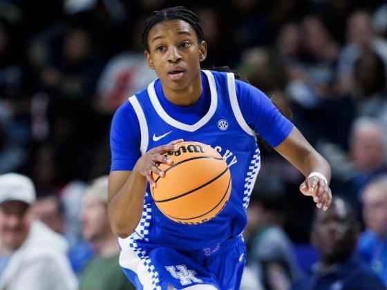 Tonie Morgan, in a blue and white Kentucky uniform, dribbles the ball on the court during a game against Georgia. The background shows a crowd of spectators.