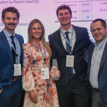 Four people dressed in formal attire stand smiling at an event. One person holds an award. A presentation screen displays company names like Apple Inc. and Microsoft Corp. behind them. The award has the Tennessee Valley Authority logo on it.