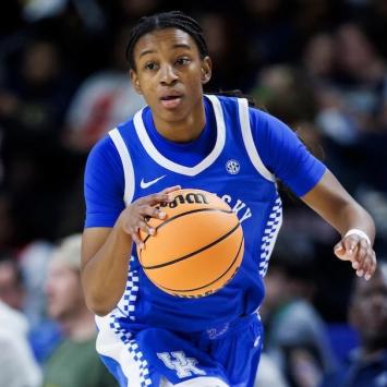 Tonie Morgan, in a blue and white Kentucky uniform, dribbles the ball on the court during a game against Georgia. The background shows a crowd of spectators.